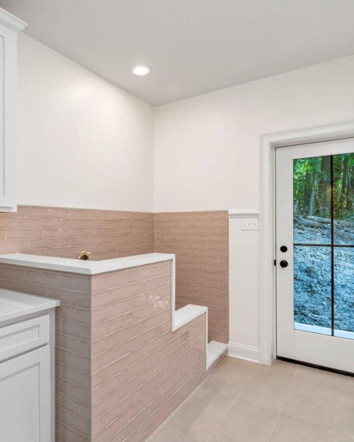 Soft blush brick tile mudroom wash station with step-up design from @milestonehomespgh. Durable, stylish pet bath area.