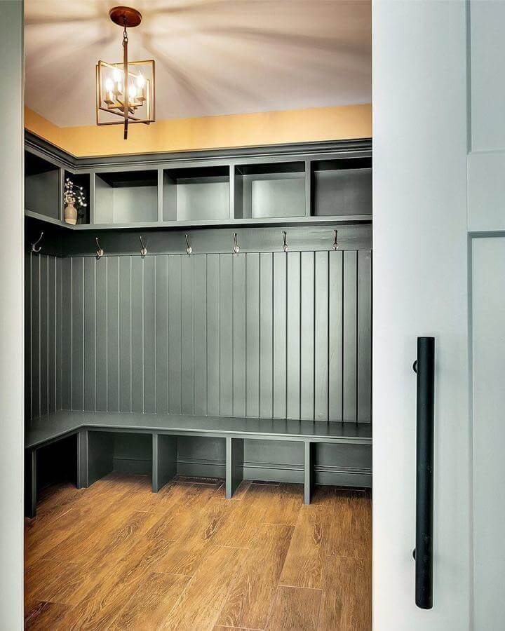 Warm wood-look tile planked flooring in a mudroom from @kadilakhomes. Durable and inviting storage space with dark cubbies.