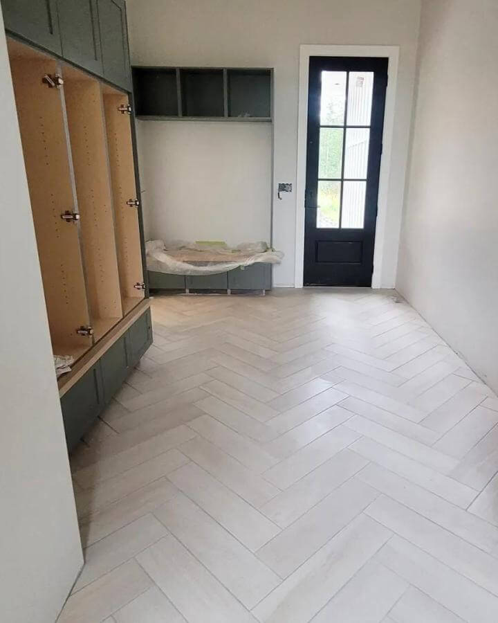 White herringbone porcelain tile floor in mudroom with black door and green cabinets from @our_dream_in_the_country showcasing durable stylish entryway flooring.