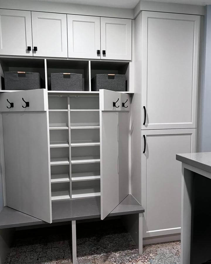 White modern cabinetry mudroom shoe storage ideas with fold-out racks and black hooks from @ids_ccc. Organized and stylish space with fabric bins and bench.