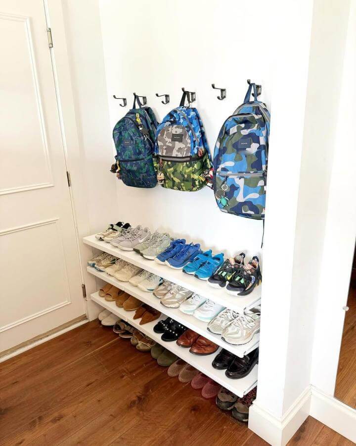 White wooden Elfa shelving with colorful camo backpacks hung on hooks in a tidy entryway corner by @creativeorganizingbychristine for shoe organization.