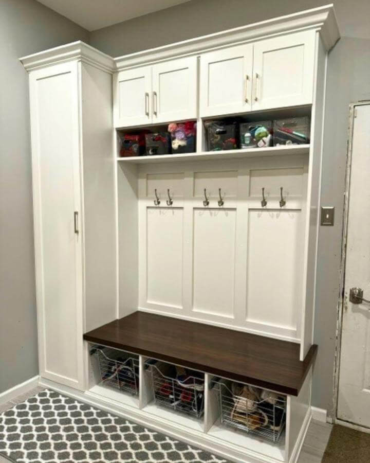 White built-in mudroom storage with dark wood bench and chrome pull-out shoe baskets from @closetsbydesign.pa.de for organized entryway footwear and accessories