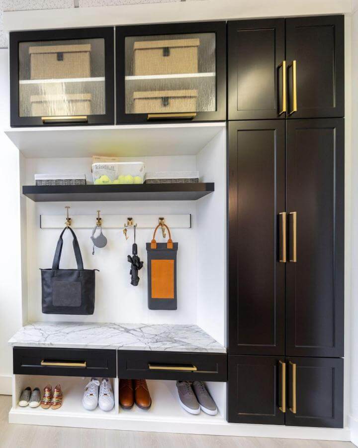 Black mudroom cabinetry with brass hardware and marble bench from @bethesda_closets featuring built-in shoe cubbies and elegant storage solutions.