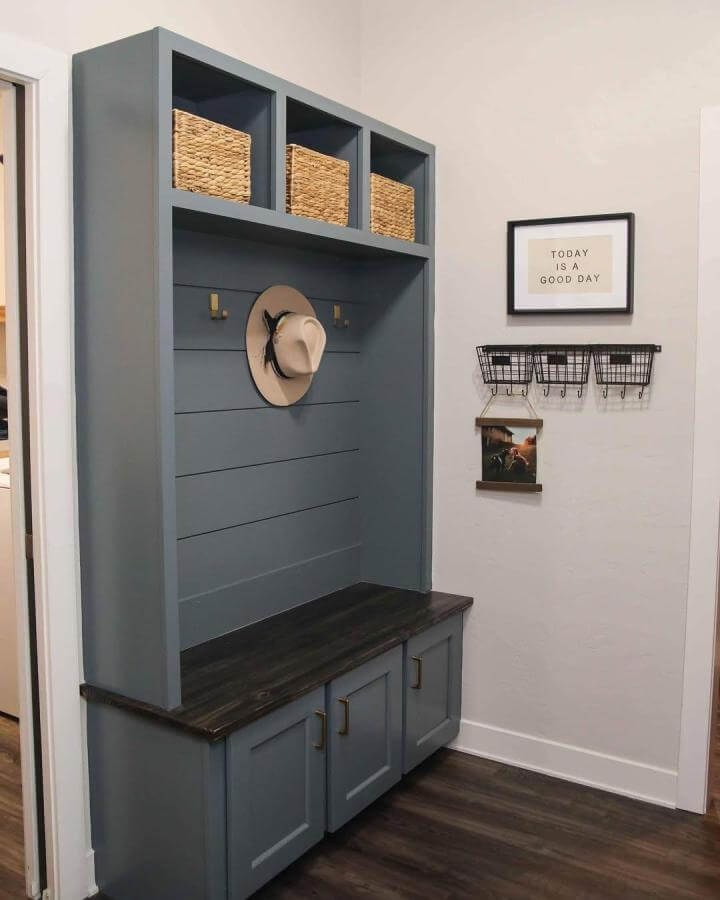 Blue-gray wooden bench with shiplap backing and natural woven baskets in cubbies for shoe organization by @buildhappywitherin. Rustic yet modern style.