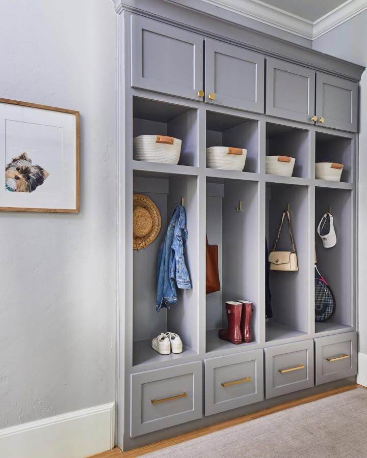 Gray built-in cubbies with brass handles and leather baskets in a mudroom by @melbeaninteriors showing organized shoe and gear storage.