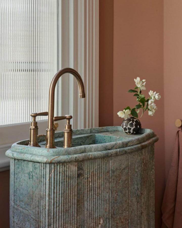 green marble sink with brass fixtures and peach wall by @smartanson natural stone bathroom ideas with textured vertical lines and elegant design