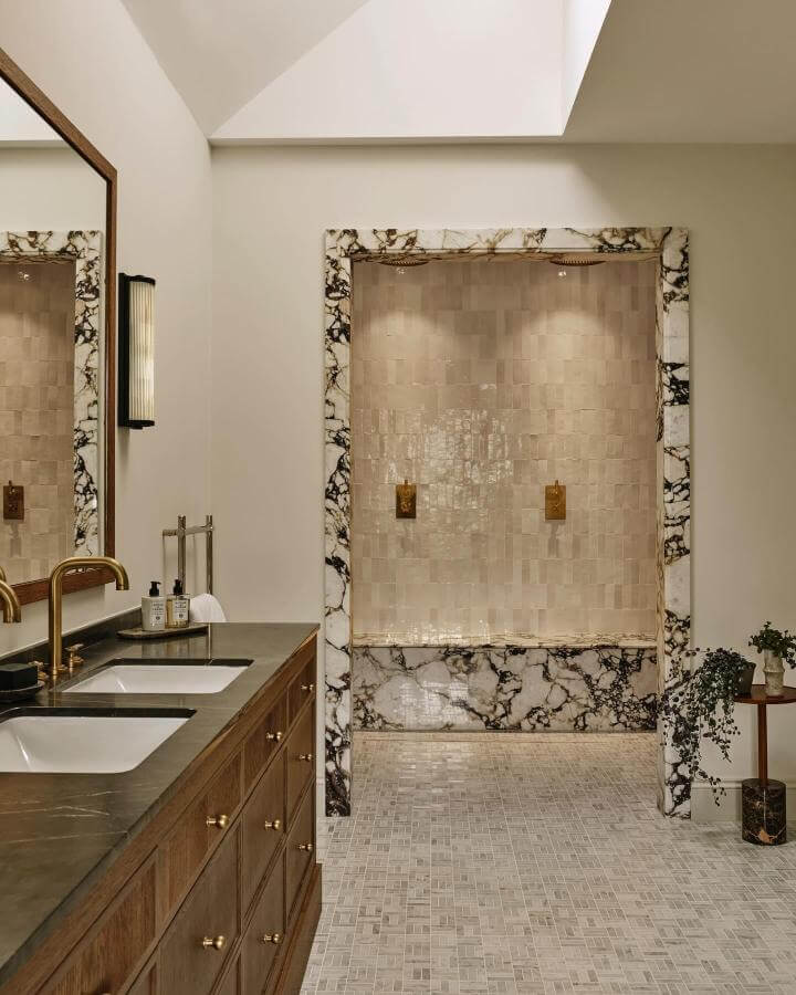 White and black veined marble-framed shower with beige tiles and wood vanity from @horwoodphoto natural stone bathroom ideas.