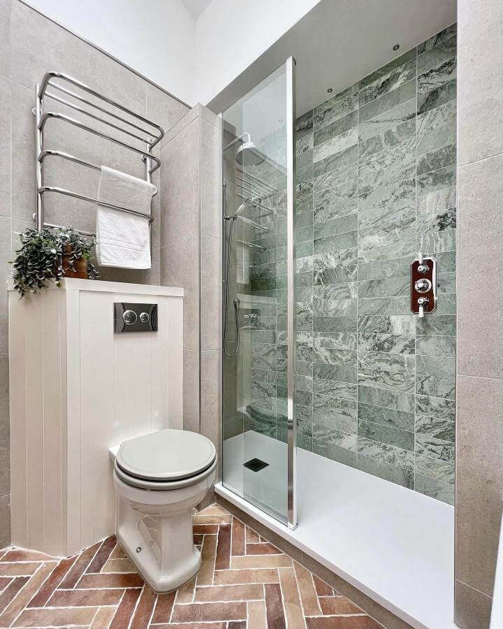 Green marble wall shower with terracotta herringbone floor natural stone bathroom ideas from @thetapend.design. Sleek and warm contrast.