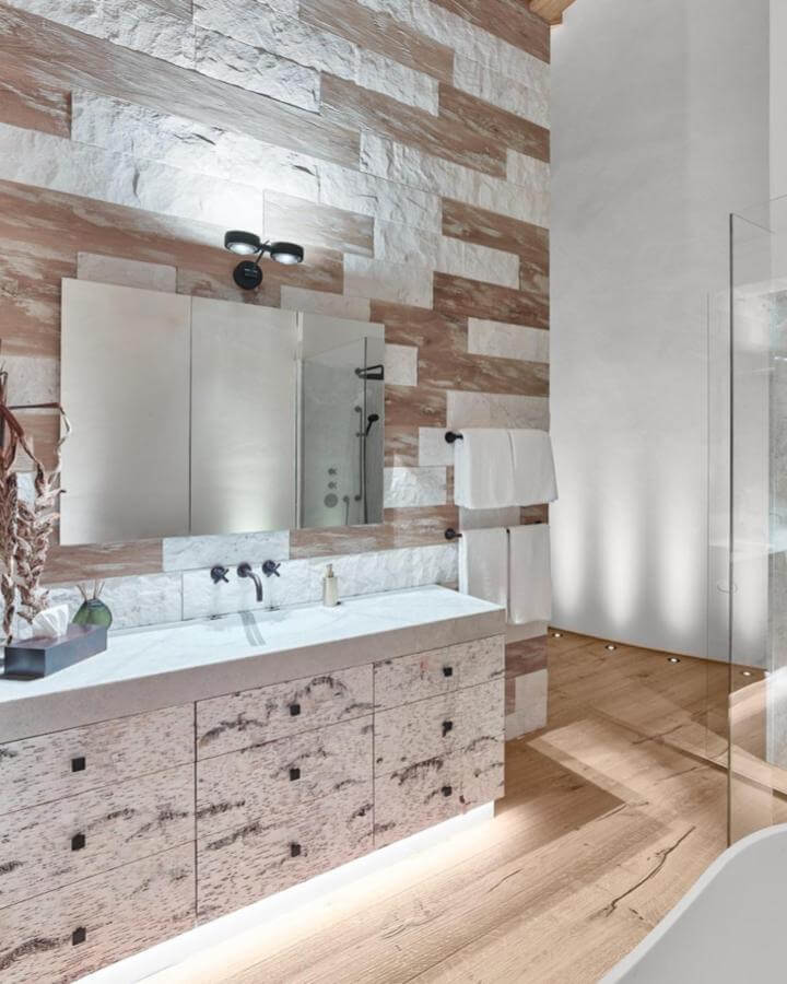 Cream and taupe textured natural stone wall and rustic wood vanity bathroom from @widmerwohnen with soft natural stone bathroom ideas lighting.