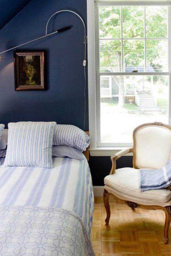 Striped bedding with bold navy accent wall in bedroom from @benjaminmooreuk. Moody navy bedroom ideas inspire calm and style.