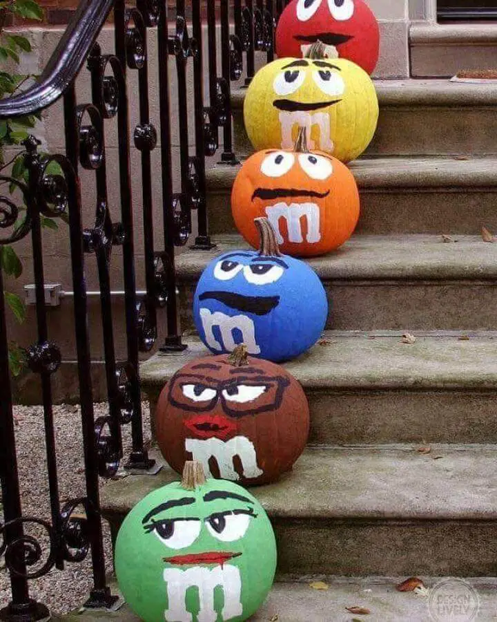 Colorful M&M character painted pumpkins from @crafty_morning lined up on concrete steps for Halloween decorating.