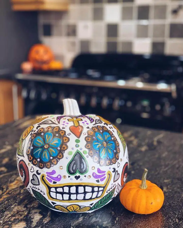 Painted sugar skull pumpkin from @cartref_hapus sits on granite countertop with colorful Day of the Dead design.