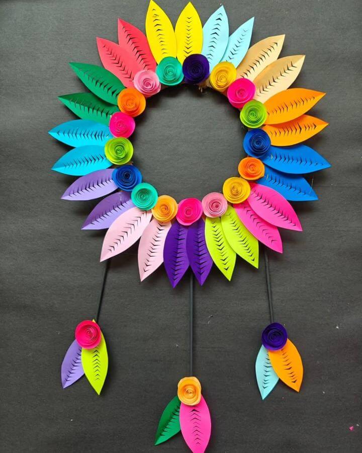 Bright multicolored paper wreath with spiral flowers and cut leaves on dark background from @creativesuu, paper crafts for adults vibrant and playful design.