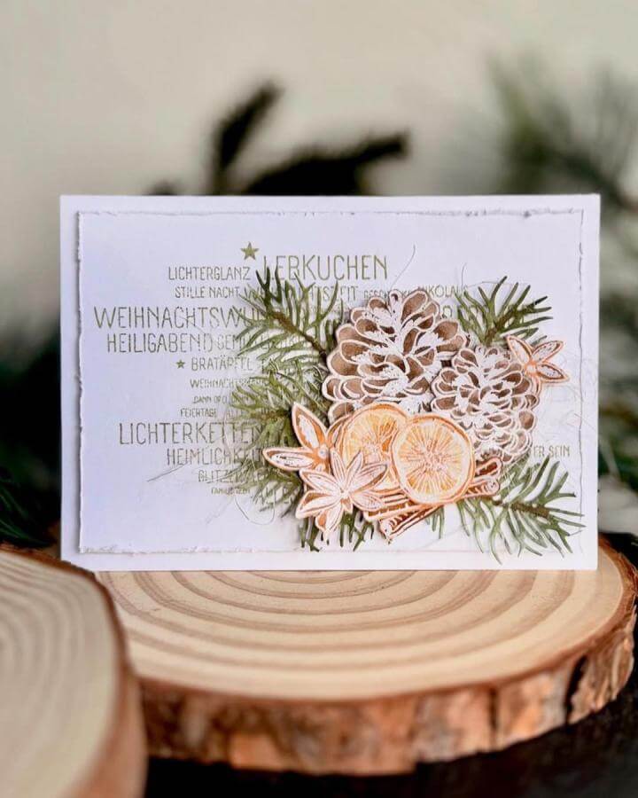 White card with layered paper pinecones, orange slices, and green pine sprigs in paper crafts for adults by @li.l.a12. Festive textured handmade card.