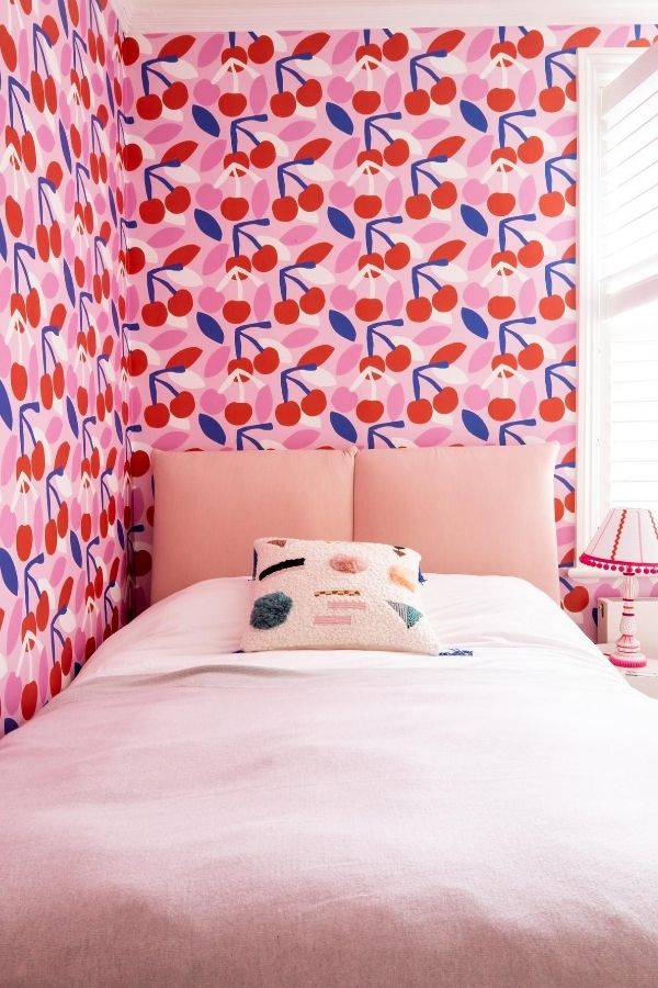 Vibrant pink bedroom featuring cherry-patterned wallpaper and playful decor.