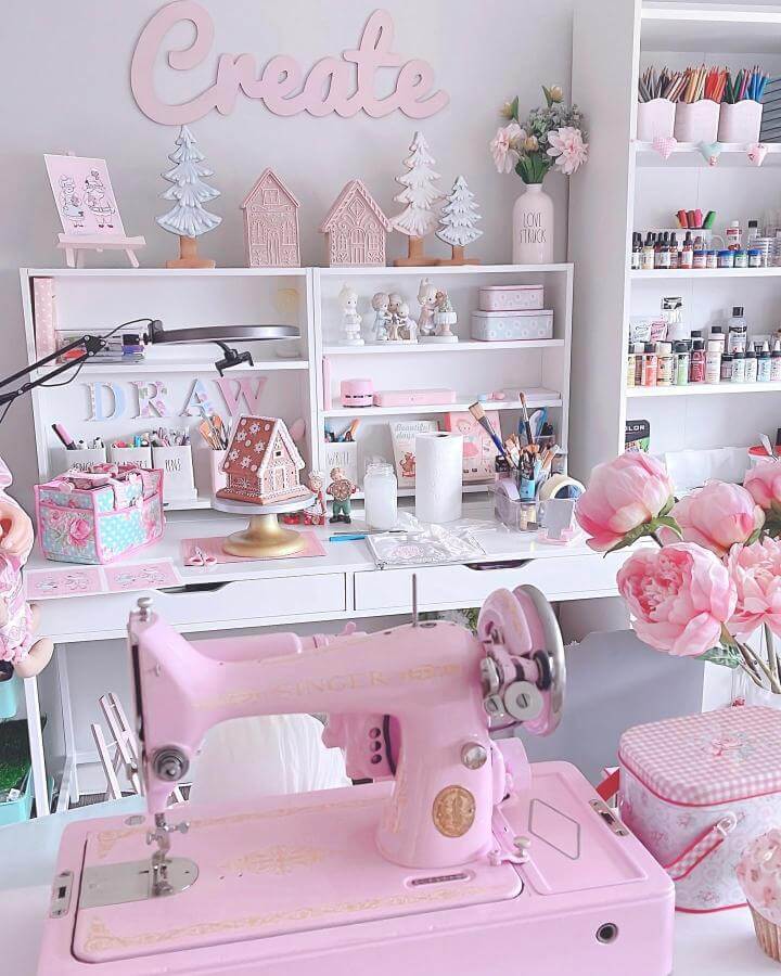 Pink vintage sewing machine in a craft room styled with white shelves and floral decorations for pink craft room ideas.