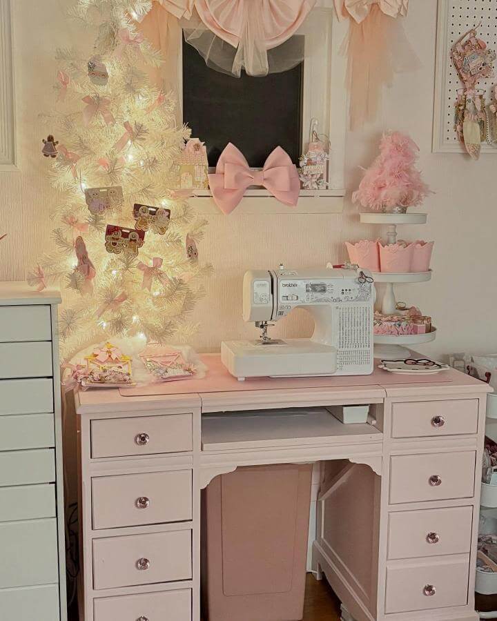 Soft blush pink sewing desk with white sewing machine and pastel craft decorations in a cozy workspace by @whimsy.designs.usa.