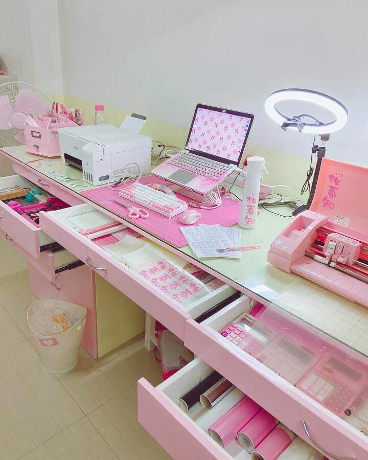 Pink-themed craft desk with organized drawers and vinyl rolls by @pinkcottagechic featuring pastel accents and a ring light for crafting.