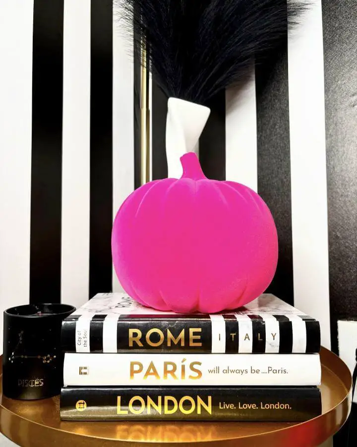 Glossy magenta pumpkin decoration from @iamstarvibez. Styled on black and white striped books for modern Halloween contrast.