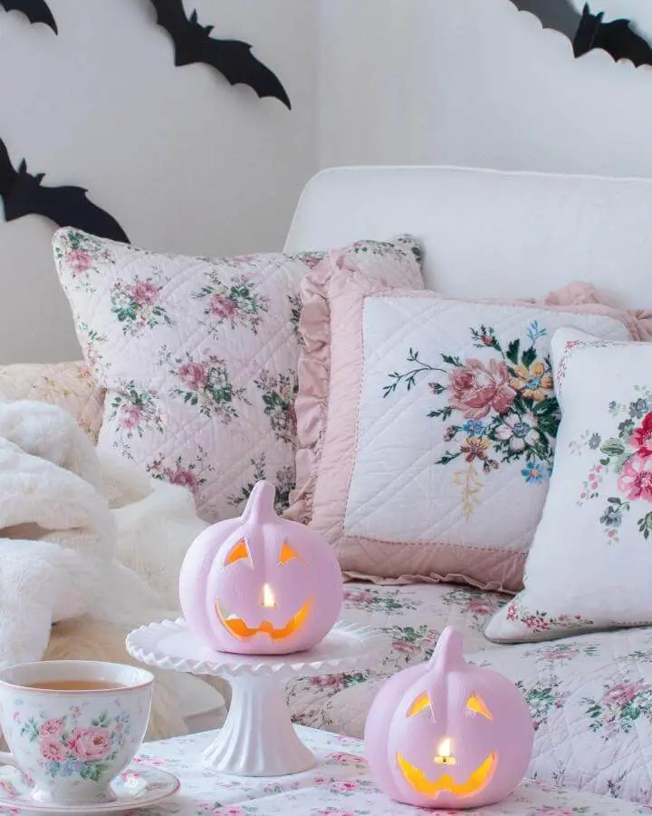 Pastel pink jack-o'-lanterns on floral bedding from @enjoyeveryday79. Glowing carved pumpkins create whimsical bedroom Halloween atmosphere.