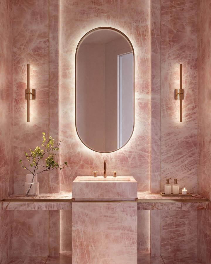 Pink marble powder room with gold fixtures and backlit oval mirror from @triplegroup_. Luxurious pink powder room ideas with elegant lighting and natural accents.
