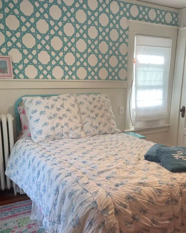 Teal geometric trellis wallpaper bedroom from @1904square. White trim and floral bedding complete the coordinated look.
