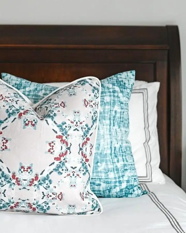 Mixed floral and textured throw pillows from @merinda_studio. Teal and coral patterns against dark wood headboard.