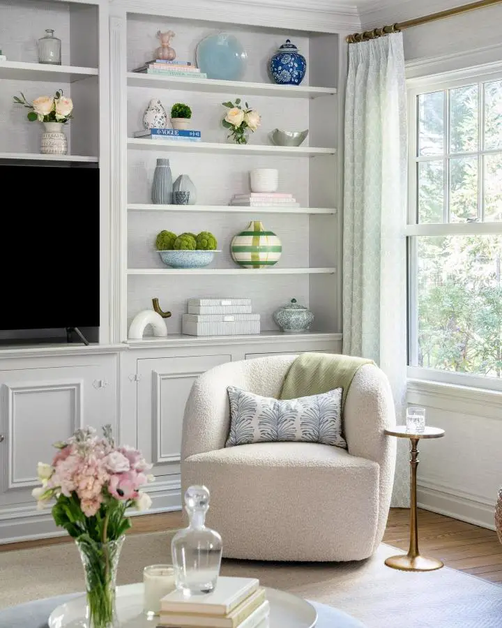 White built-in shelving unit with blue ceramics and green accents showcasing preppy living room ideas from @kristenkellscreative.