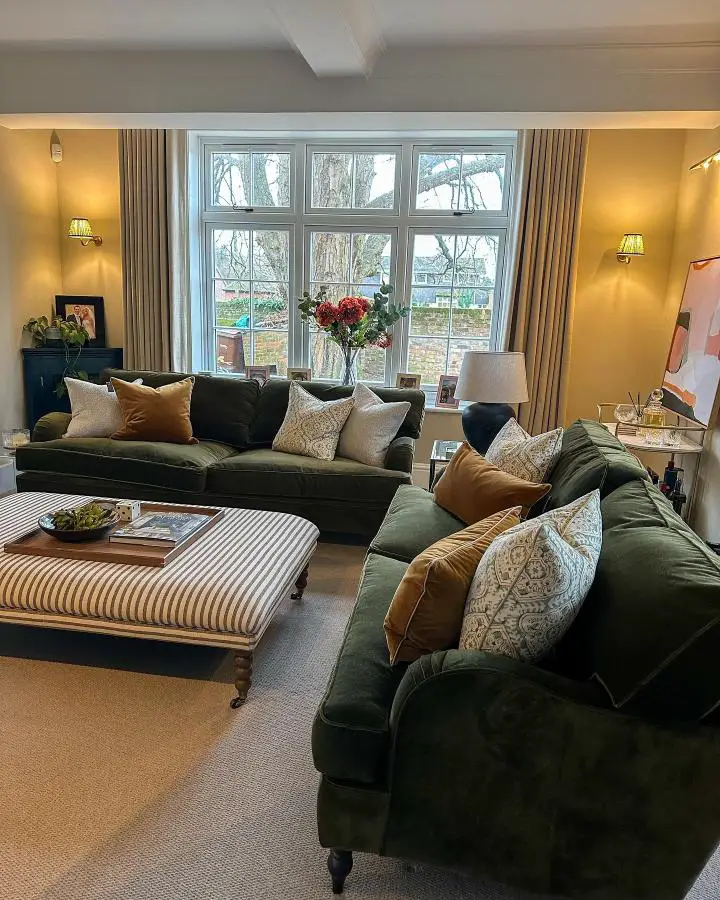 Sophisticated forest green velvet sectional from @justalittlebuild. Rich textures and warm yellow walls create cozy atmosphere.