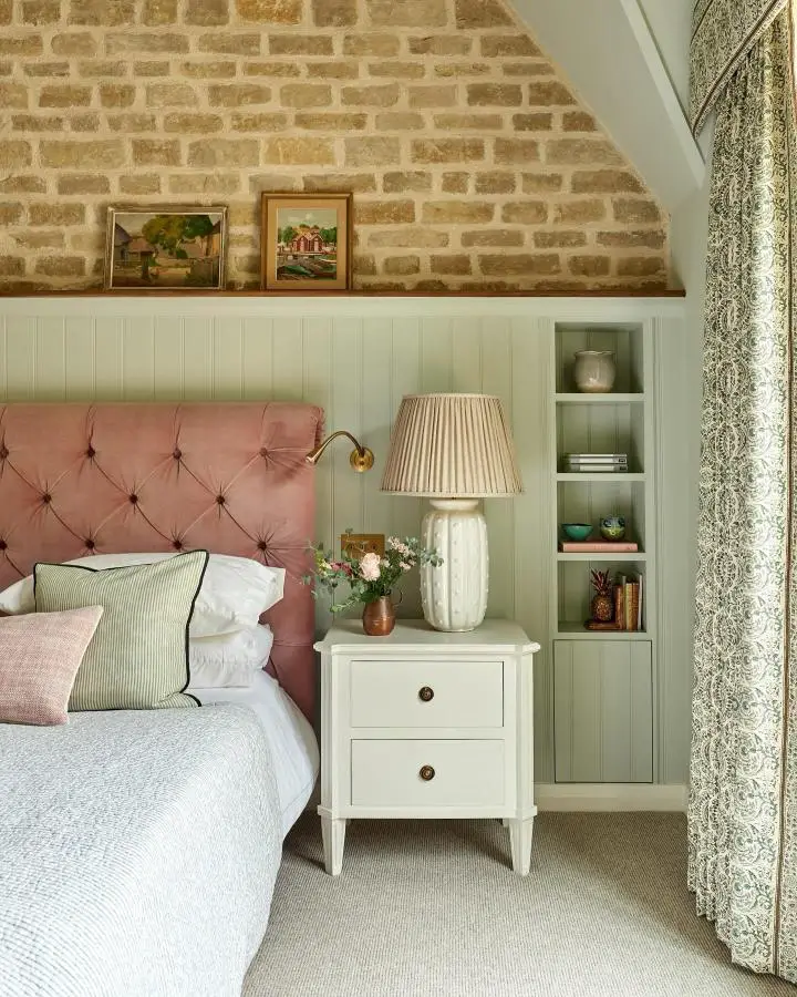 Dusty pink velvet headboard from @johnstonparkeinteriors. Sage green built-in shelving and exposed brick create cozy cottage style.