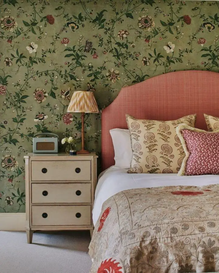 Sage green floral wallpaper bedroom from @georgiewykehamdesigns. Coral headboard showcases timeless pretty bedroom ideas with botanical patterns.