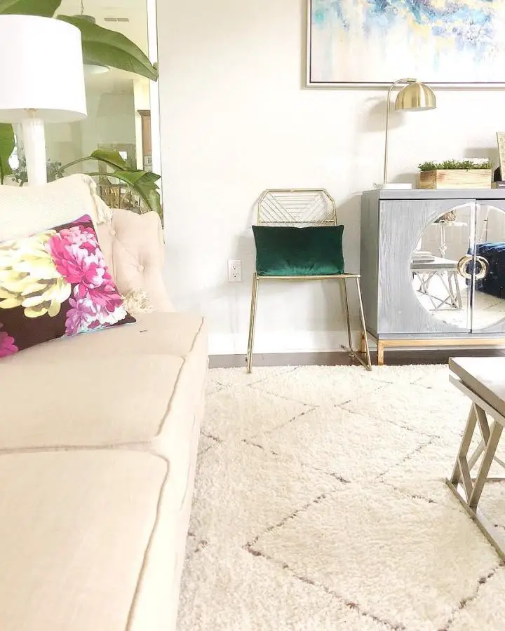 Emerald velvet accent chair with brass frame from @house_of_joy_interior_design. Positioned next to mirrored cabinet in bright living space.