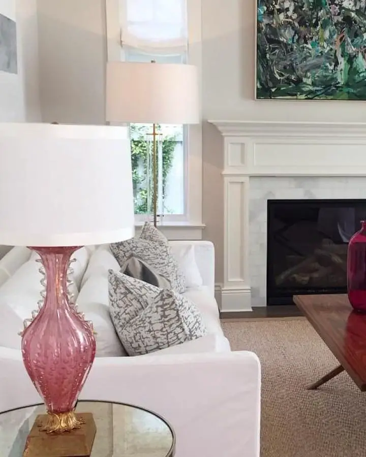 Coral glass vase on round coffee table from @evarsanderson. White sofa with textured pillows beside fireplace.