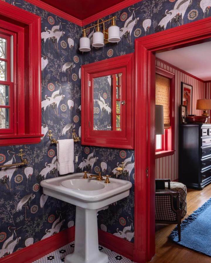 Red trim and crane wallpaper in powder room from @mindtgap showing bold red powder room ideas with vintage sink and brass fixtures.