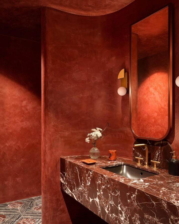 Rich red plaster walls with marble vanity and brass fixtures in a red powder room by @gregnatale simple floral accent brightens space