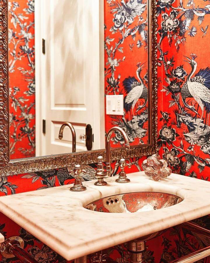 Red wallpaper powder room with ornate gold mirror and marble countertop from @jenamidesigns. Elegant crane and floral design.