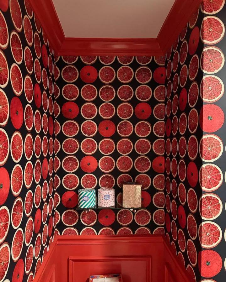 Red grapefruit wallpaper and glossy red trim in a powder room from @annieelliottdesign. Vibrant red powder room ideas with playful citrus pattern.