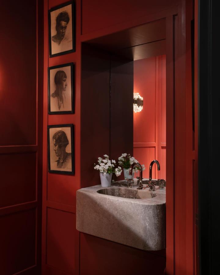 Red walls with sculpted stone sink and vintage sketches in a powder room by @charles_zana creating bold red powder room ideas ambiance.
