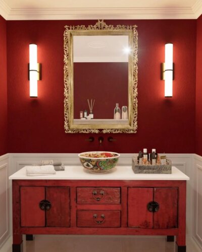 Red walls with vintage rustic vanity and gold ornate mirror from @smartrenovationdubai. Dramatic and cozy red powder room ideas.