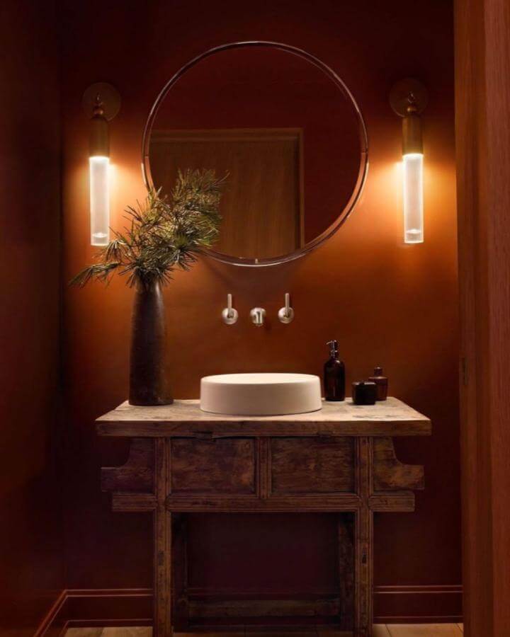 Rusty red walls with rustic wood vanity and warm lighting in a red powder room ideas design from @blacksquarebuilders creating cozy elegance