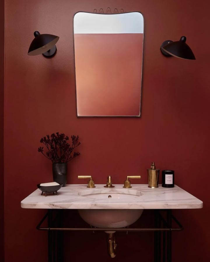 A matte red powder room with gold fixtures, white marble sink, and minimalist black wall sconces from @mirandaand.co creating warm bold red powder room ideas.