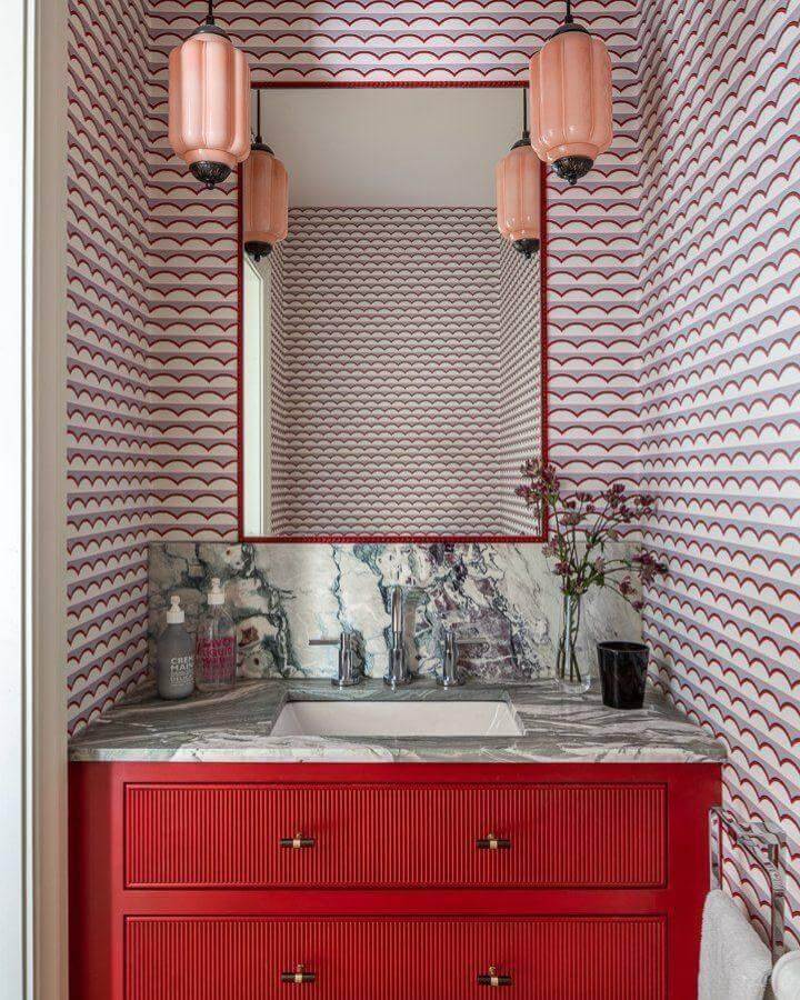 Red vanity with scallop patterned wallpaper and pink pendant lights in a stylish powder room from @shoptrask creating unique red powder room ideas.
