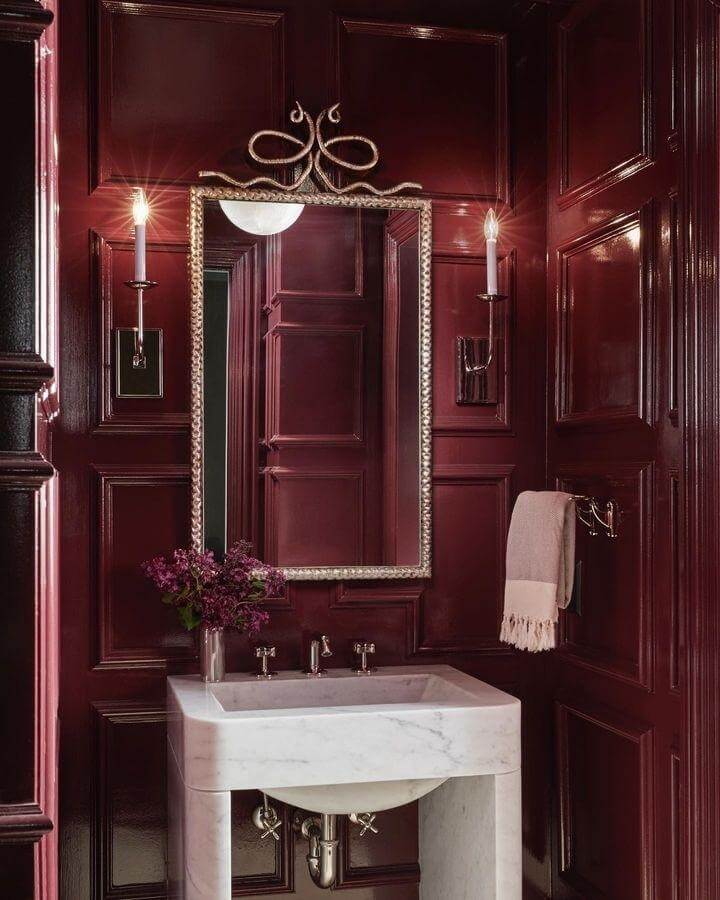 Glossy deep red lacquered walls and marble sink in an elegant red powder room ideas setup by @themartshowrooms. Vintage silver mirror and soft lighting included.