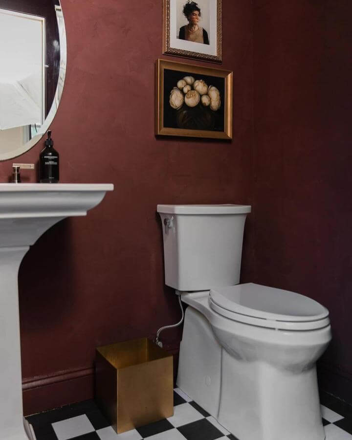 Deep red textured walls and black-and-white checkered floor in a powder room from @portolapaints with classic art and gold accents creating elegant red powder room ideas.