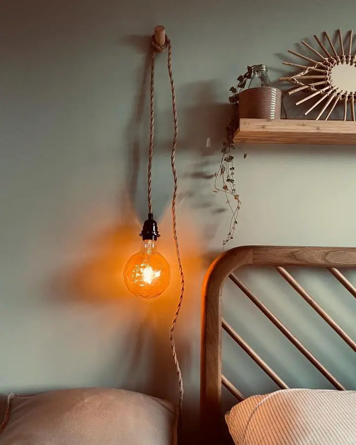 Cozy sage bedroom corner from @greystone_orchard_reno featuring warm Edison bulb lighting and natural wood textures.