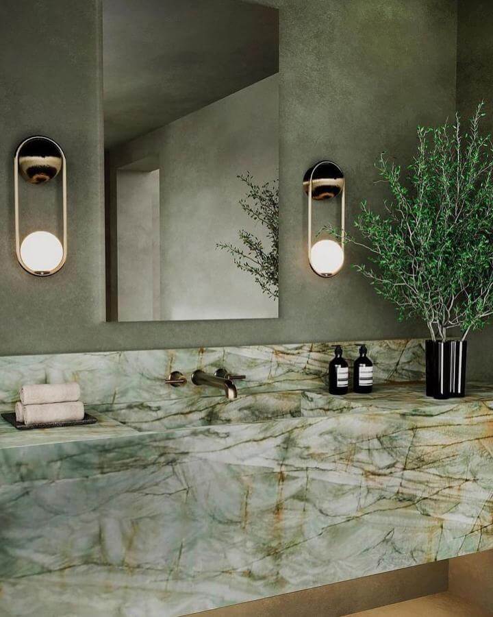 Green marble vanity with gold veins and sage walls in a powder room by @thescalecollective featuring modern lighting and fresh greenery.