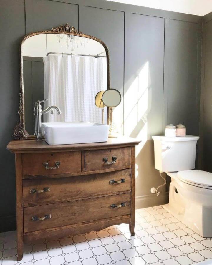 Vintage wooden vanity with ornate mirror and sleek white basin in sage green powder room by @rosewoodhomes.design. Light fills the space highlighting textures and classic charm.