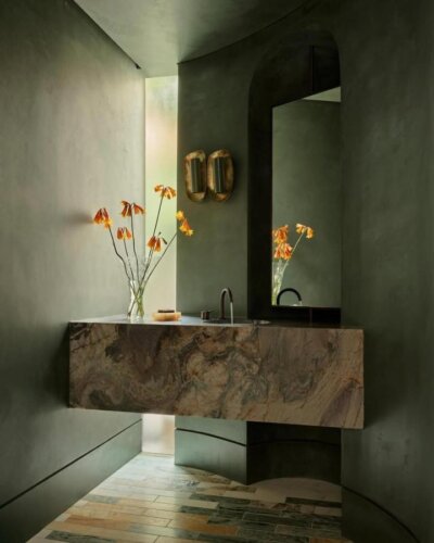 Sculptural marble sink and matte sage green walls in powder room from @thescalecollective with warm orange flowers and minimalist faucet
