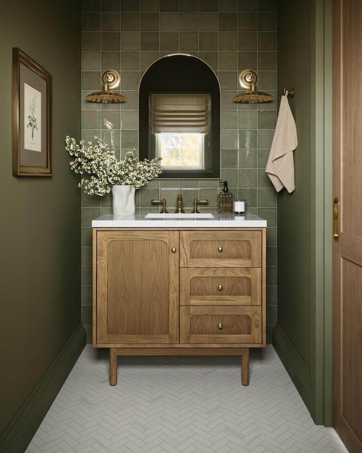 Sage green tiles and warm wooden vanity in a powder room from @edward.martin. Glossy tiles and brass accents create cozy charm.