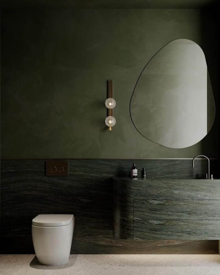 Sage green powder room ideas featuring curved stone vanity and organic-shaped mirror from @dsgn_consulting with brass lighting.